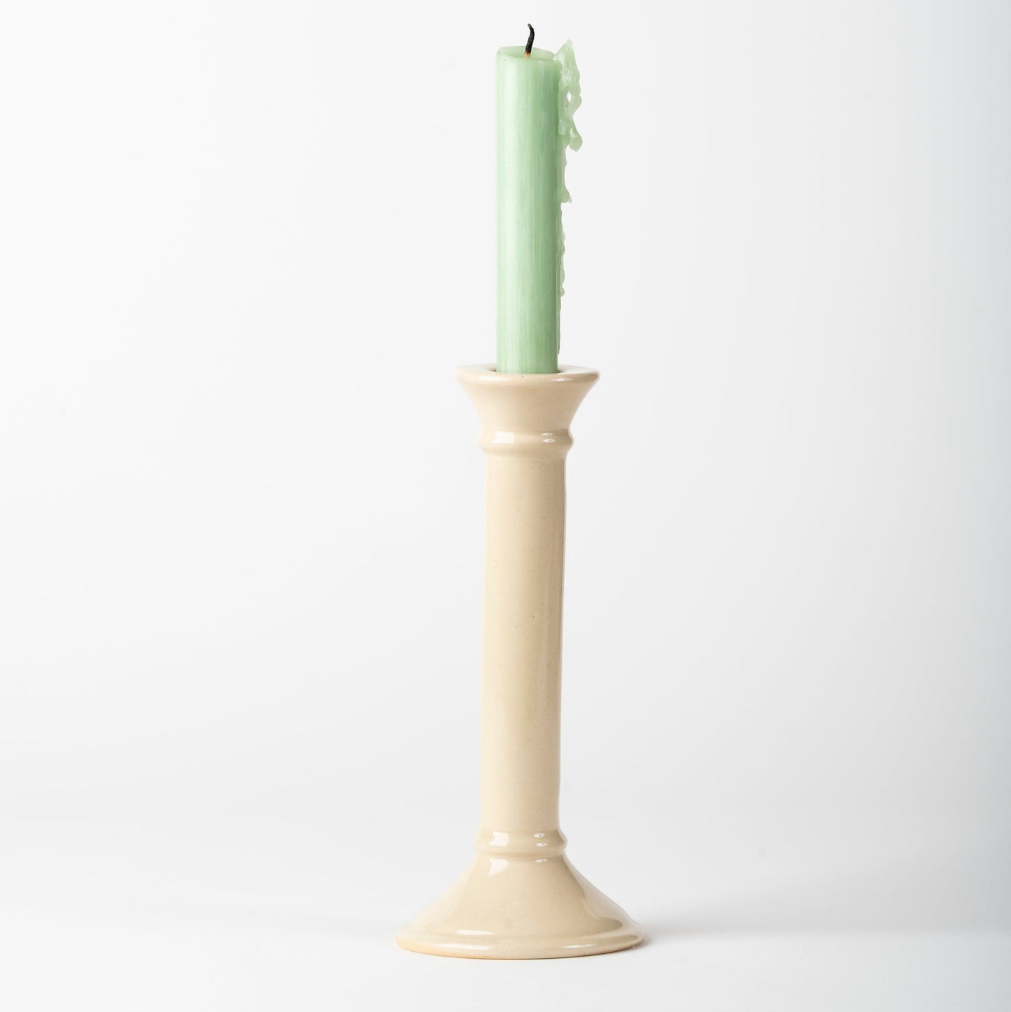 Beige candle holder with a green candle on a white background