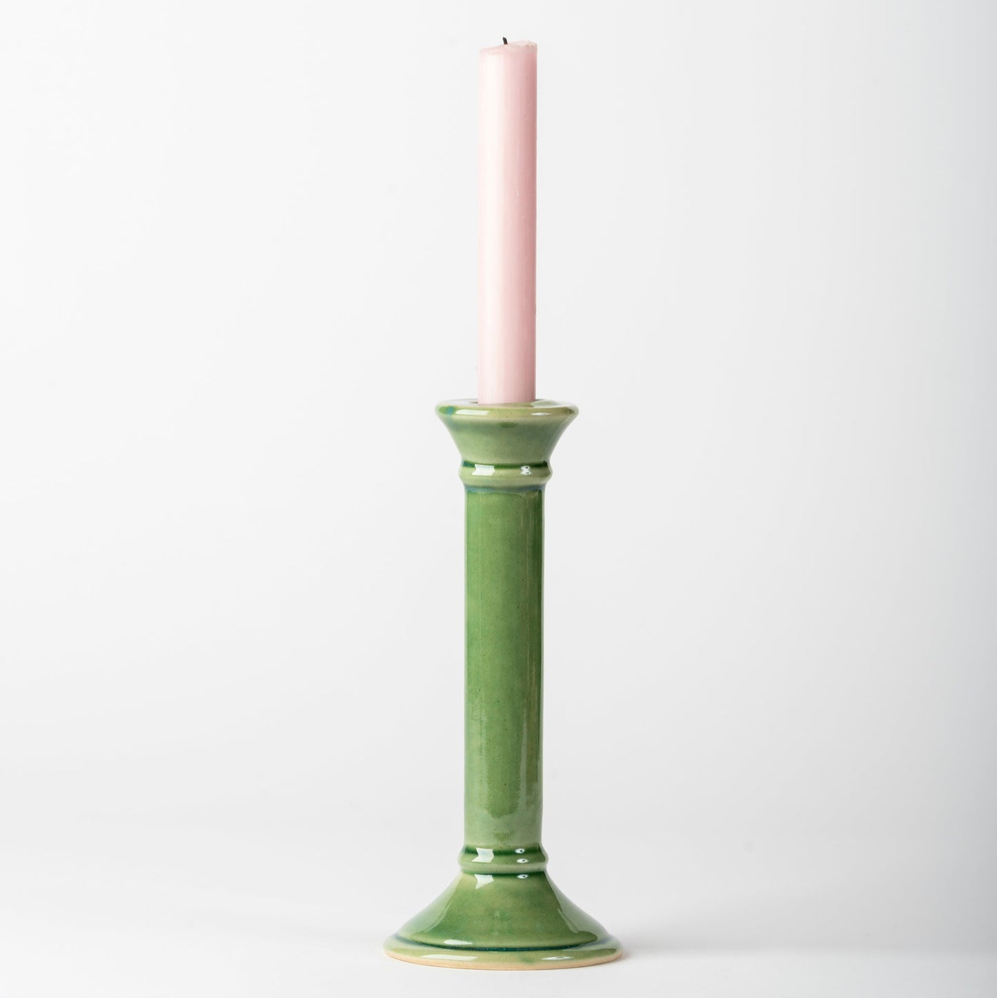 Green ceramic candle holder with a pink candle on a white background