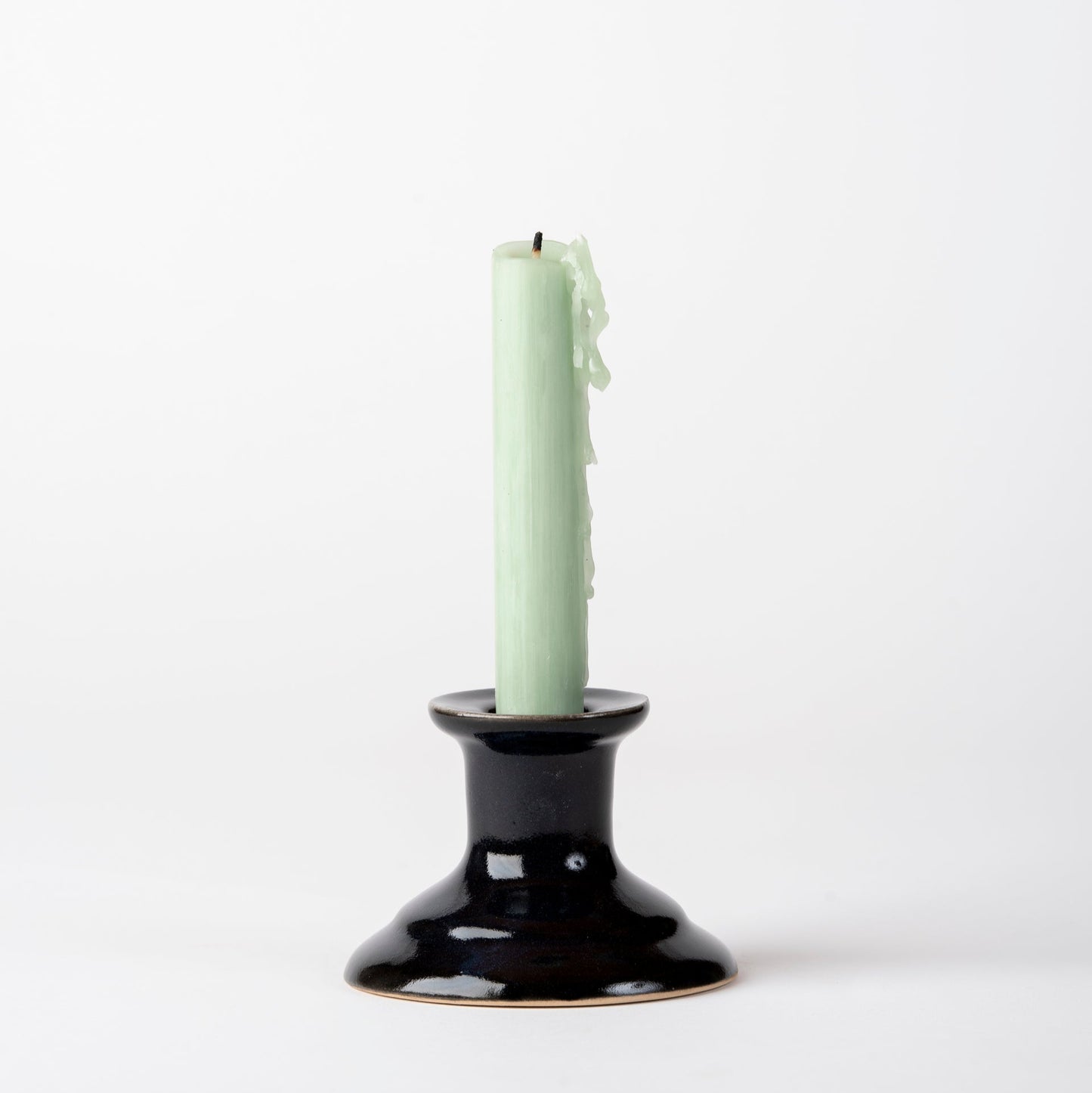 Black candle holder with a light green candle on a white background