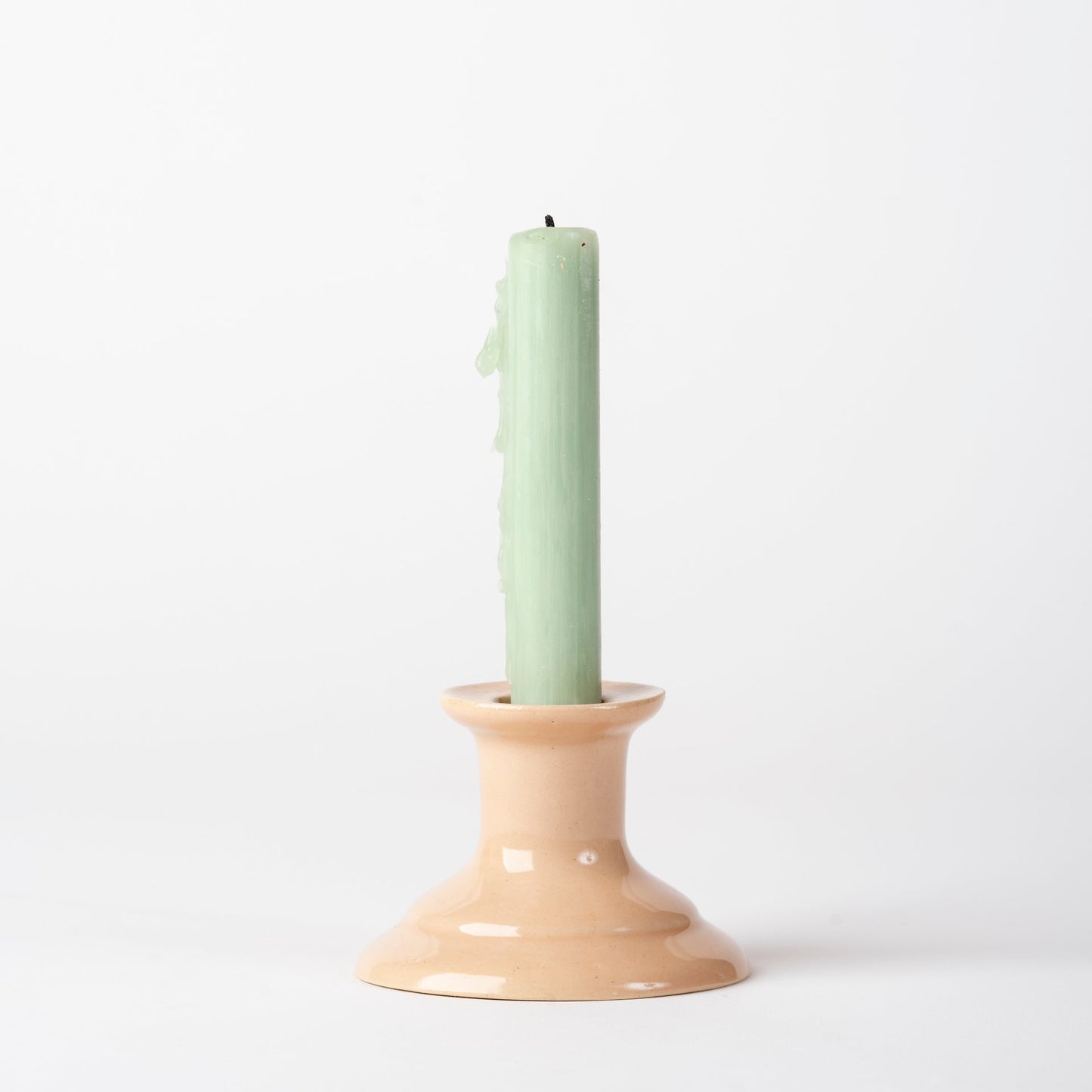 Beige candle holder with a green candle on a white background