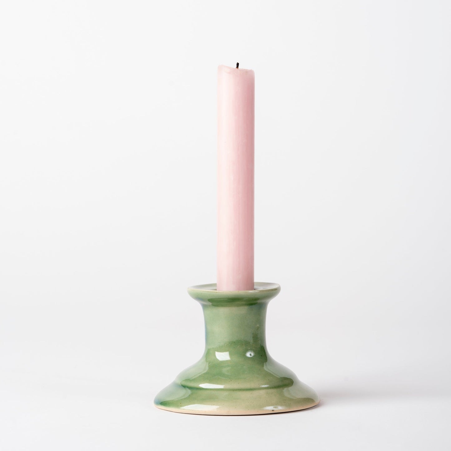 Green candle holder with a pink candle on a white background