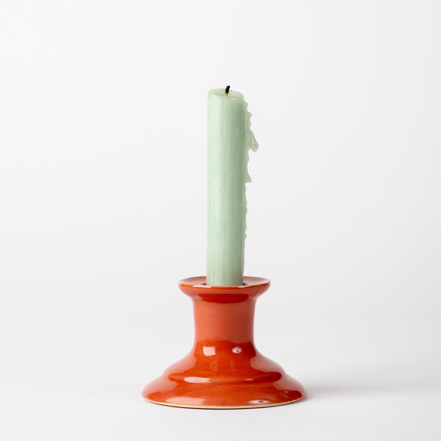 Ceramic candle holder with a green candle on a white background