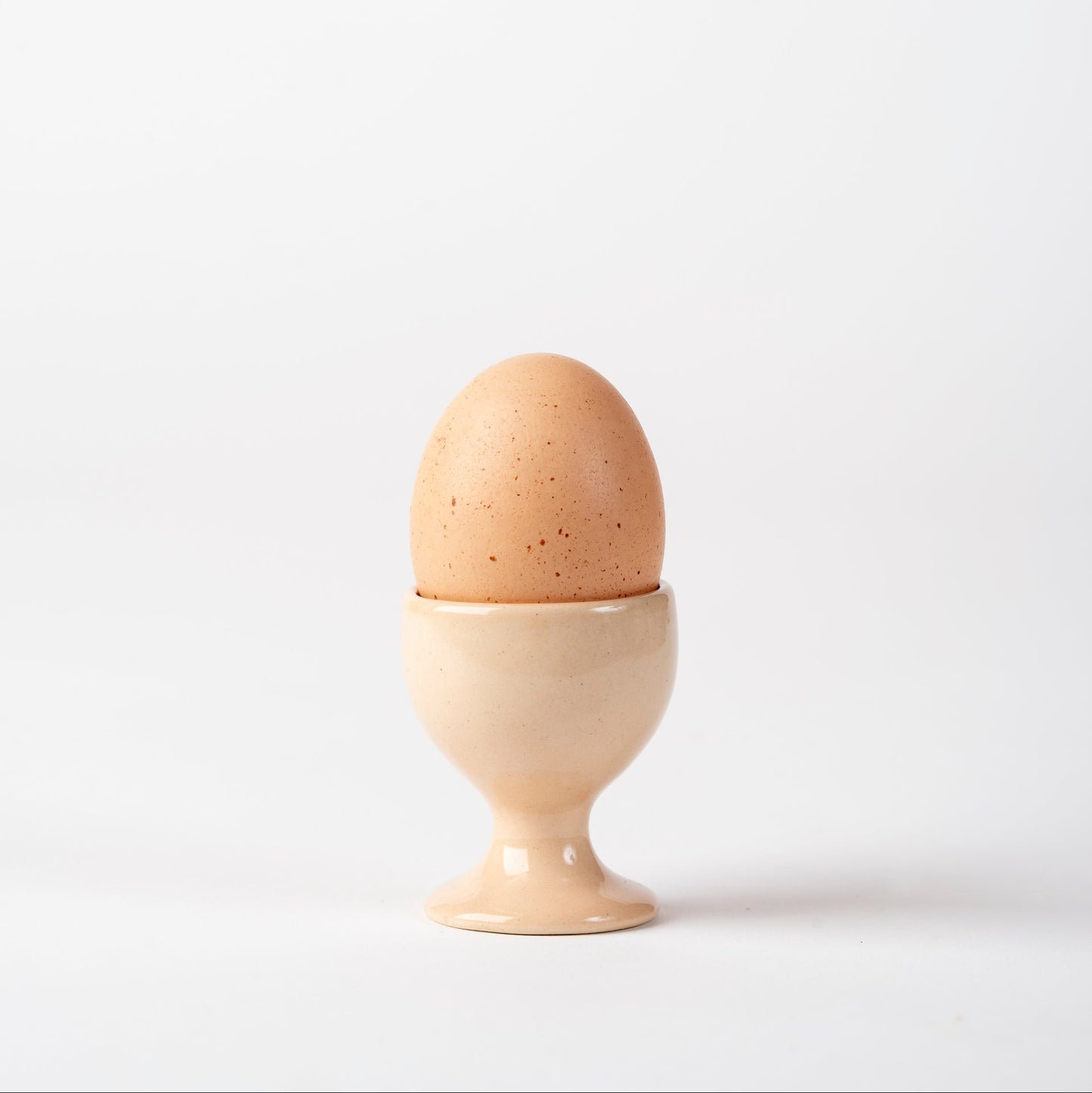 Brown speckled egg in a beige egg cup on a white background