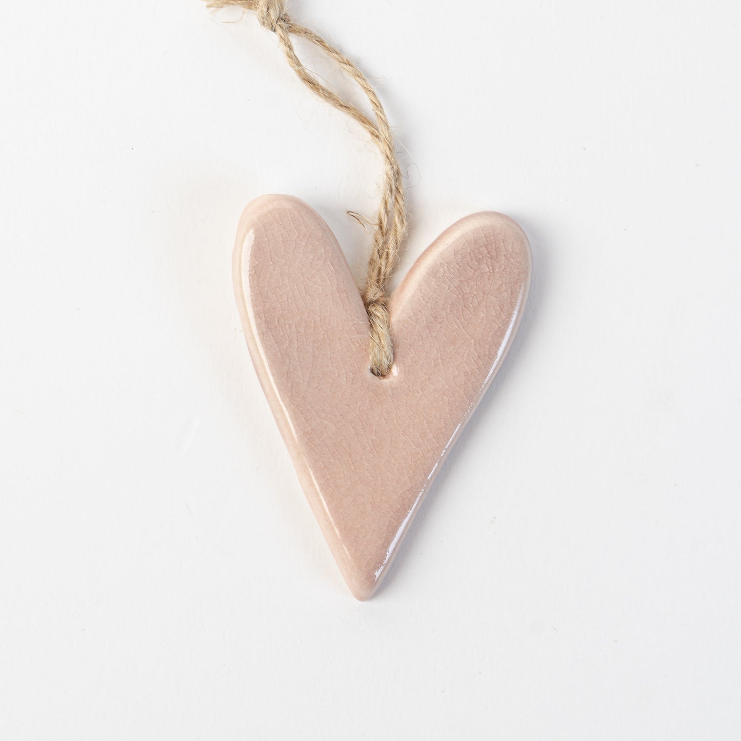 Pink Heart-shaped ceramic ornament hanging on a rope against a white background