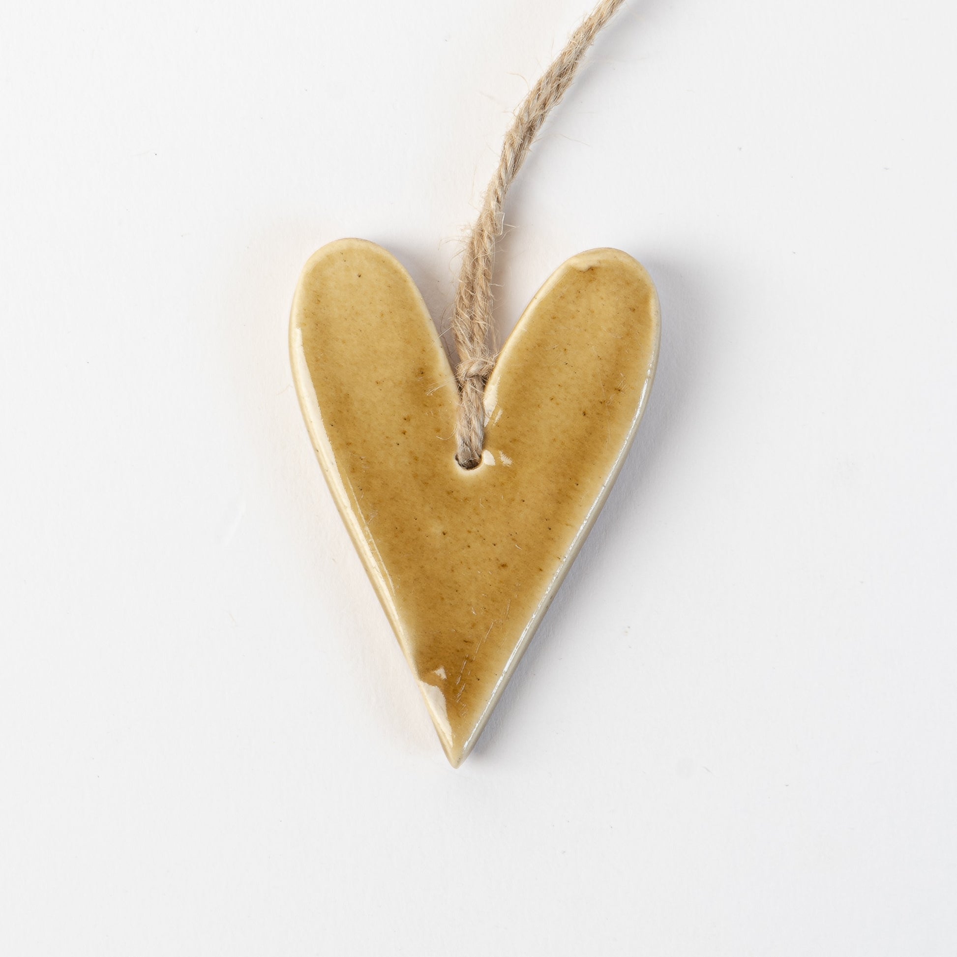 Golden yellow Heart-shaped ceramic ornament hanging on a rope against a white background