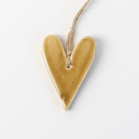 Golden yellow Heart-shaped ceramic ornament hanging on a rope against a white background