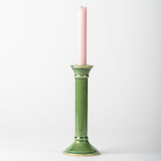 Green ceramic candle holder with a pink candle on a white background