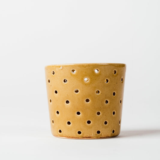 Yellow ceramic pot with holes on a white background
