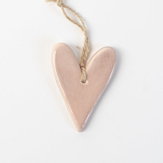 Pink Heart-shaped ceramic ornament hanging on a rope against a white background