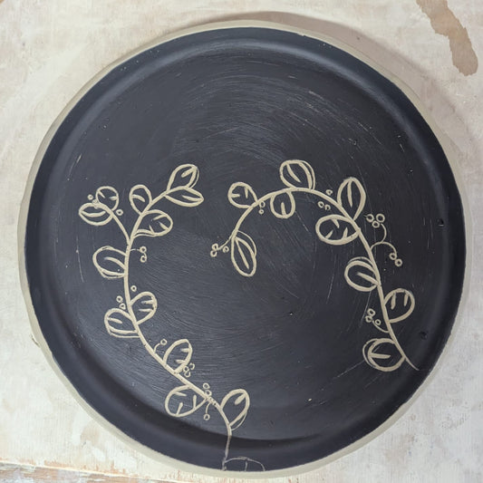 Black plate with decorative leaf pattern on a wooden surface