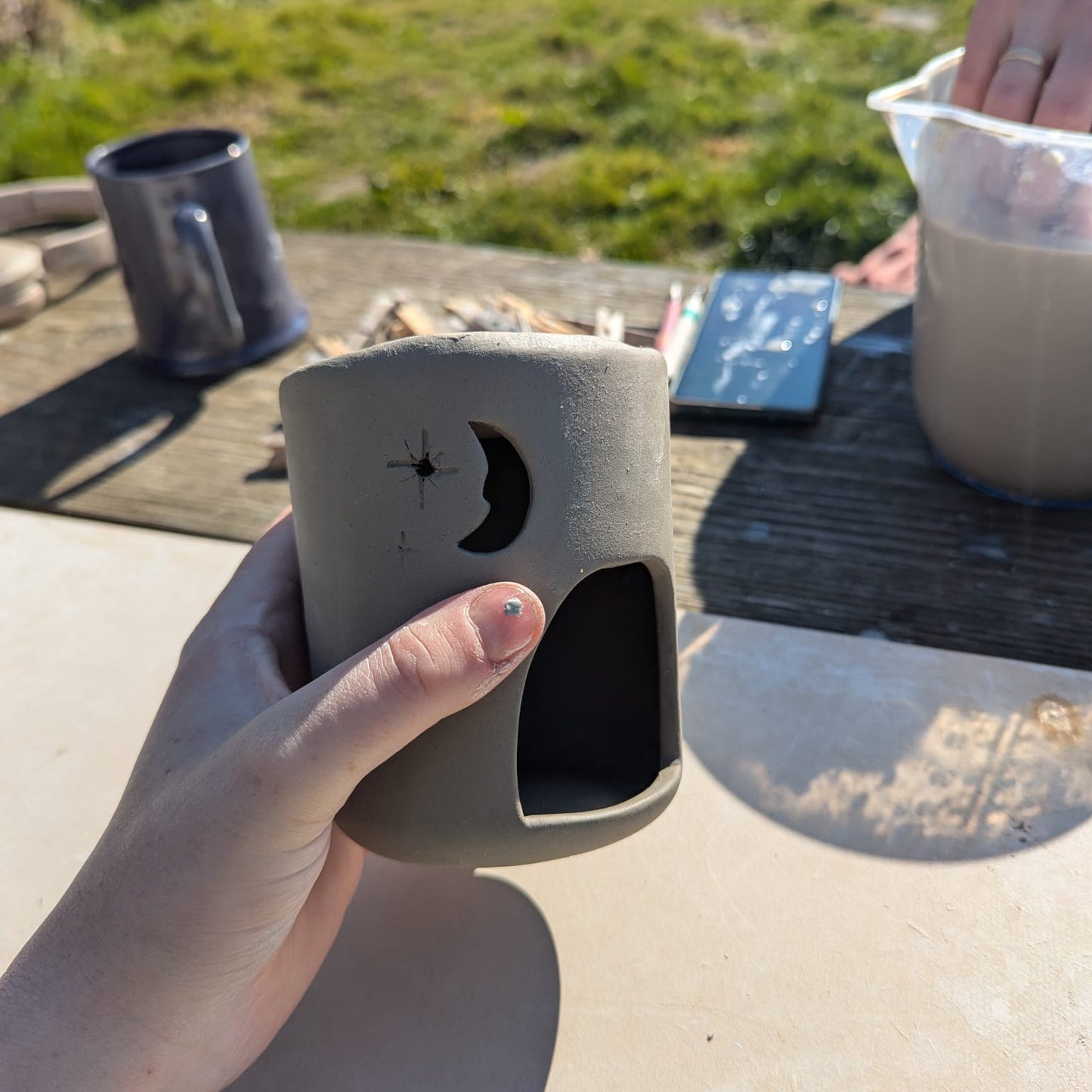 Person holding a ceramic mug with a design on a outdoor setting