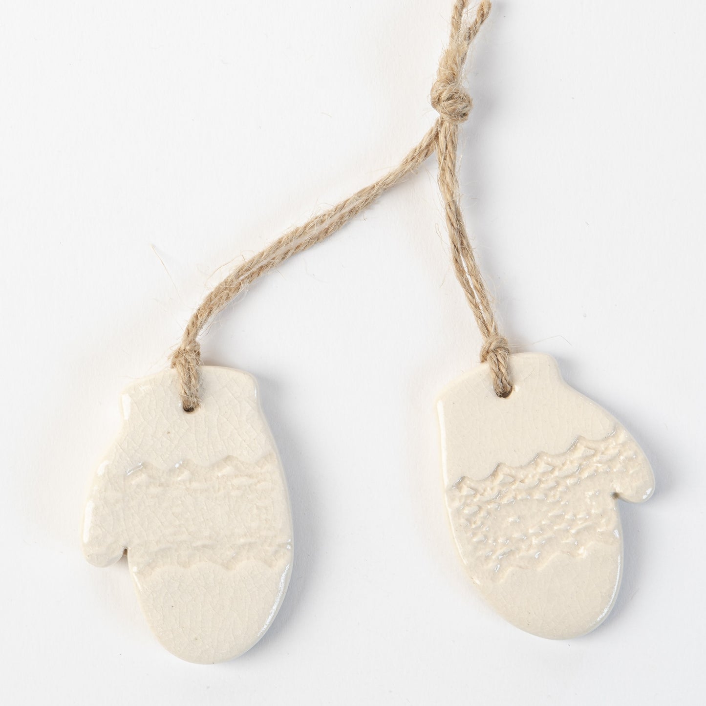 Two white ceramic mitten-shaped ornaments hanging on a rope against a light background.