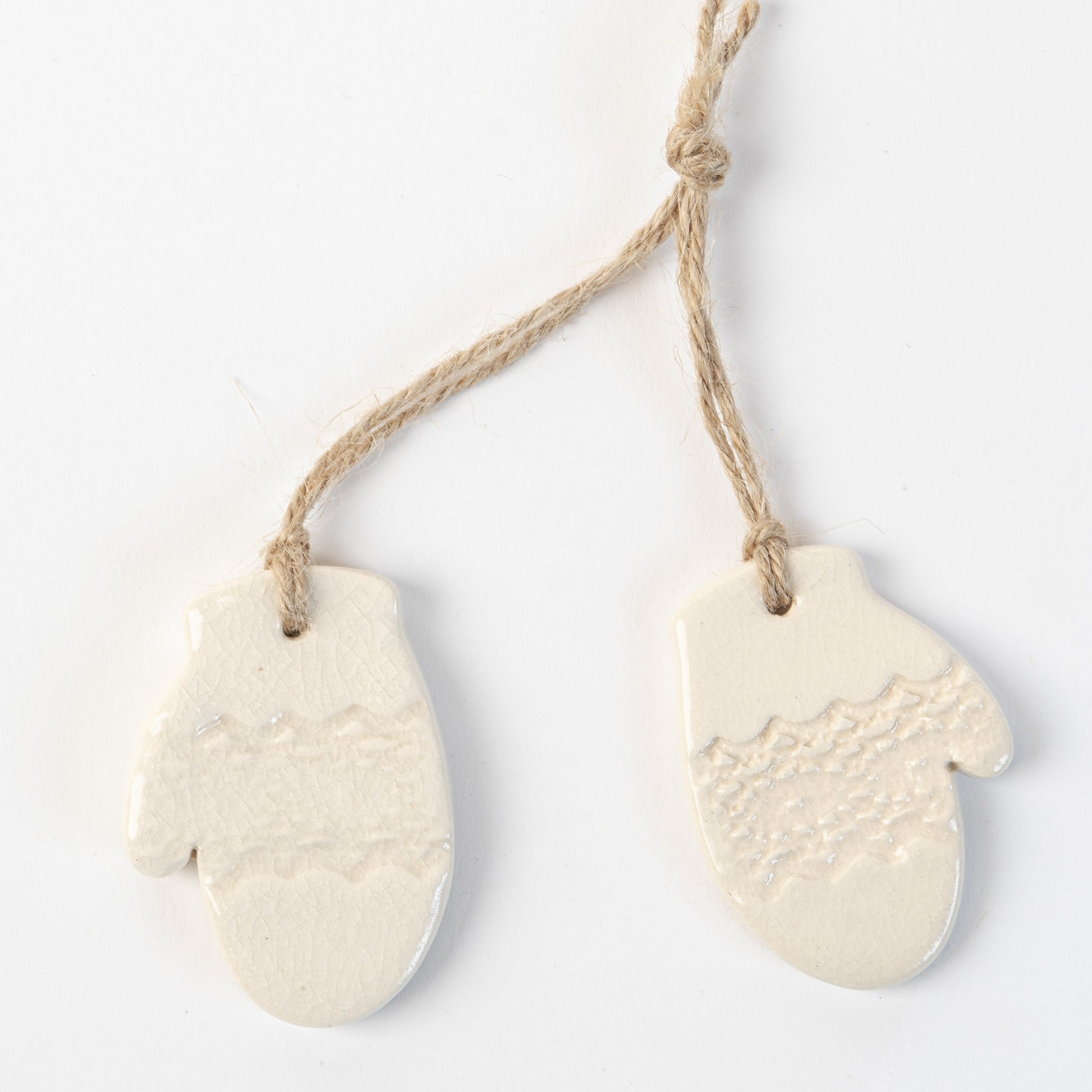 Two white ceramic mitten-shaped ornaments hanging on a rope against a light background.